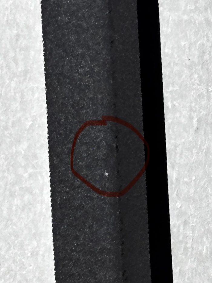 Close-up of a black printed strip with tiny pinhole voids in the ink film, circled in red