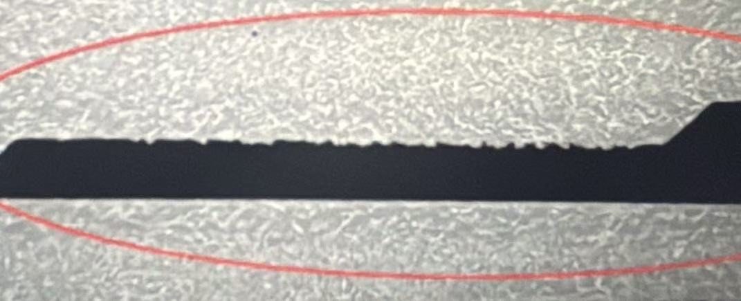 Close-up of a printed black edge showing sawtoothing: the top edge is a stair-stepped row of tiny ink teeth instead of a straight line